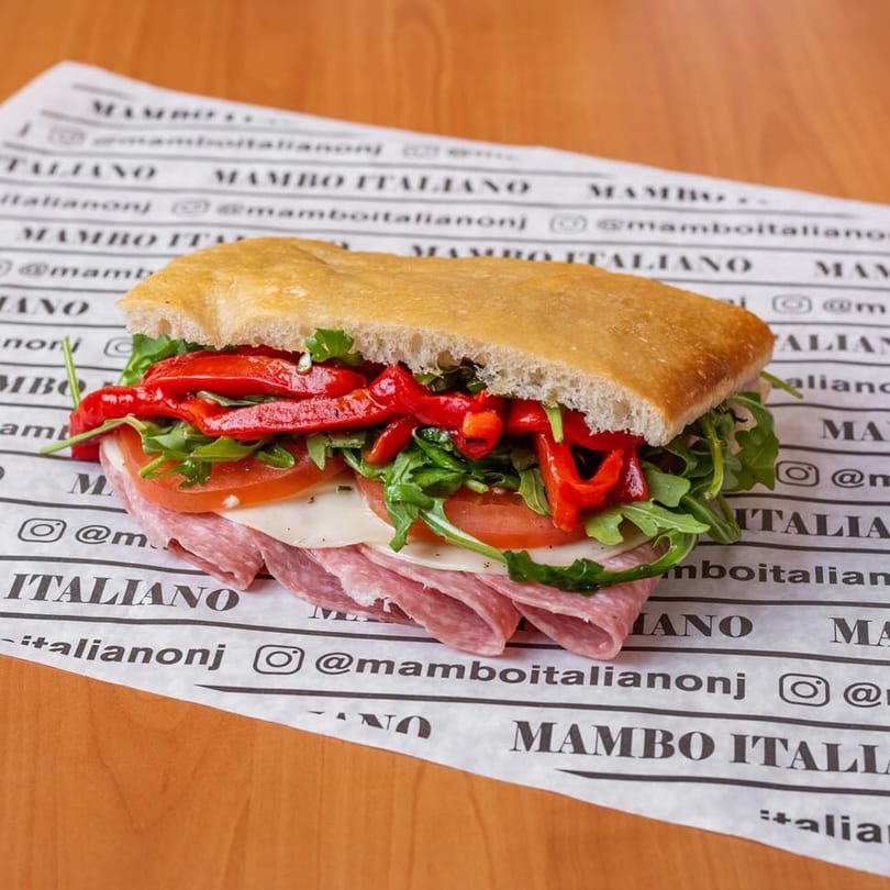 A Mambo Italiano sandwich with salami, cheese, tomatoes, arugula, and roasted red peppers on focaccia bread.